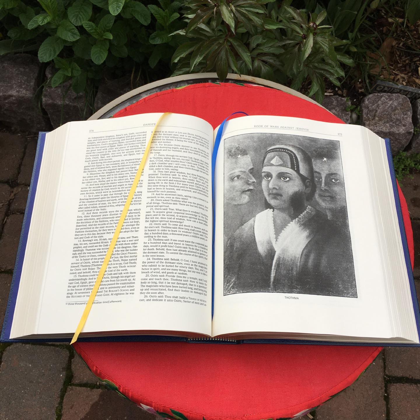 An open copy of Oahspe on a patio table. Built-in bookmark ribbons are visible, as is a portrait of Thothma.